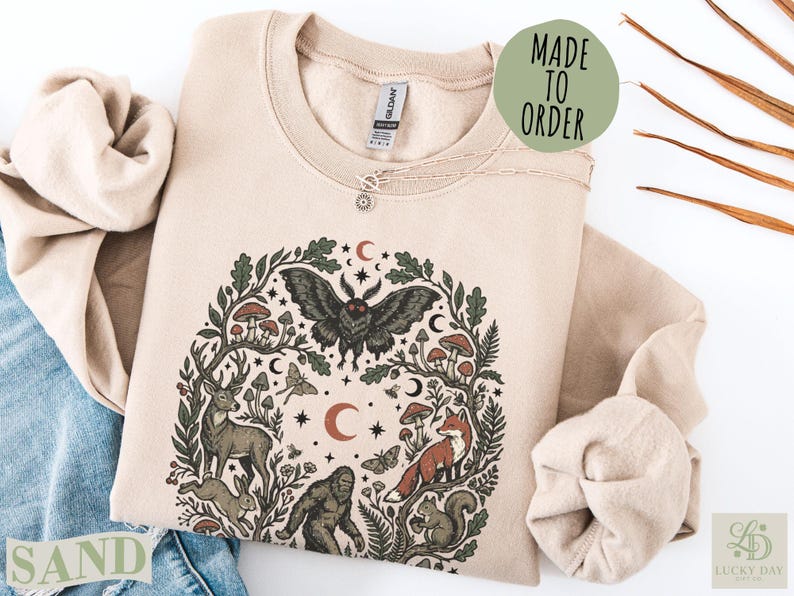 Cream sweatshirt with woodland creature and celestial art, "Made to Order" text.
