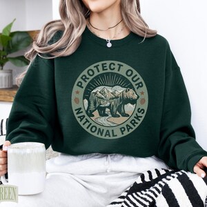 Dark green sweatshirt with "Protect Our National Parks" bear graphic.