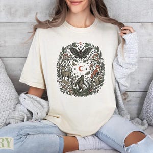 Cream t-shirt featuring a circular woodland creature and plant graphic with a butterfly at the top.