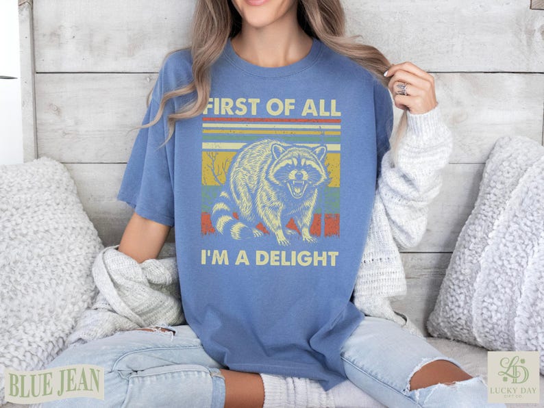 Blue t-shirt with vintage raccoon graphic and text "First of all I'm a delight."