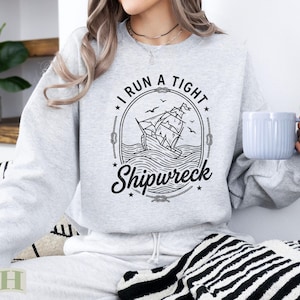 Grey sweatshirt with "I RUN A TIGHT Shipwreck" text and sailing ship graphic.