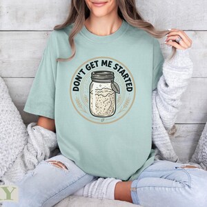 Light mint graphic tee with sourdough jar design and "Don't Get Me Started" text.