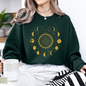 Dark green sweatshirt with gold moon phase mandala graphic.