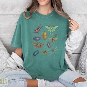 Teal t-shirt with various colorful insects including beetles, moths, and dragonflies.