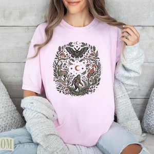 Pink t-shirt with circular forest illustration of animals and plants, featuring Bigfoot.
