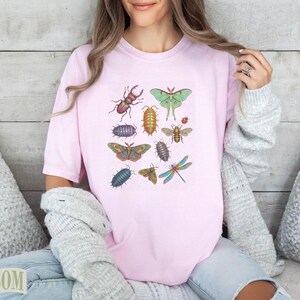 Pink t-shirt with a collage of illustrated insects including butterflies, moths, beetles, and dragonflies.