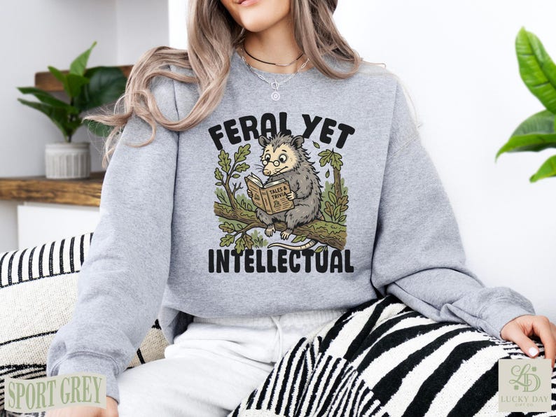 Gray sweatshirt with opossum reading book illustration and "Feral Yet Intellectual" text.
