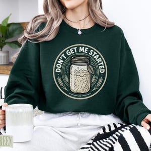 Dark green sweatshirt with "Don't Get Me Started Sourdough" text and mason jar graphic.