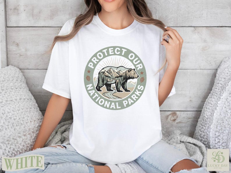 White t-shirt featuring a circular graphic with a bear, mountains, and the text "PROTECT OUR NATIONAL PARKS".