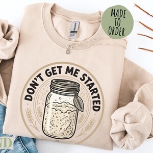 Sand colored sweatshirt with "Don't Get Me Started" sourdough jar graphic.