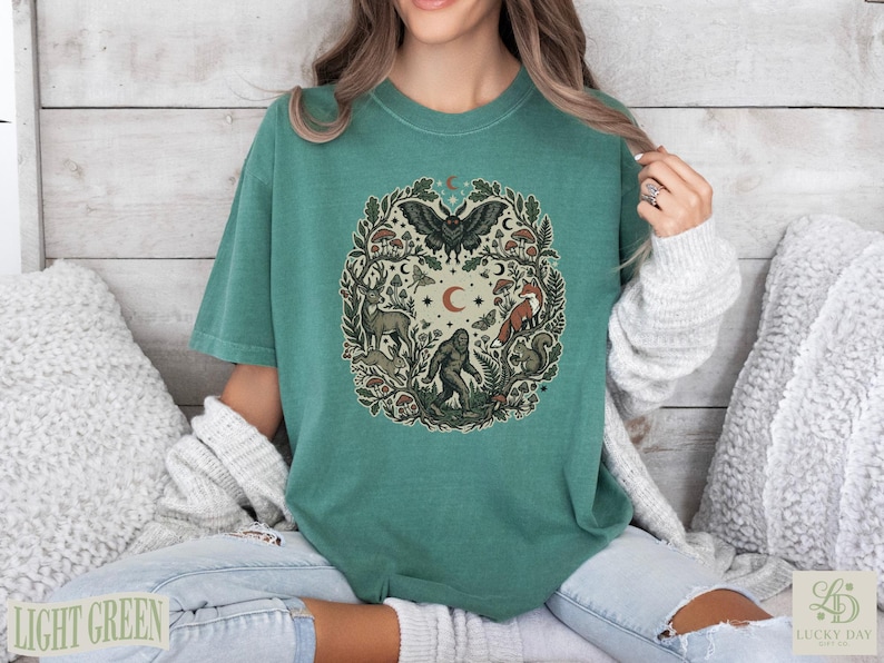 Green t-shirt with circular woodland creature and celestial graphic.