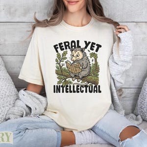Opossum reading a book titled "Feral Yet Intellectual" on a branch.