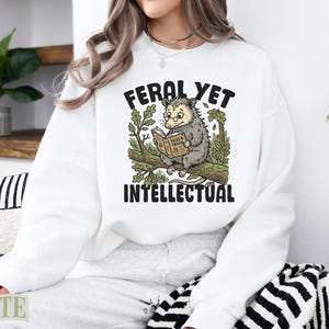 Opossum reading a book with "FERAL YET INTELLECTUAL" text.