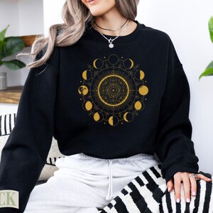 Black sweatshirt with golden celestial moon phases mandala design.
