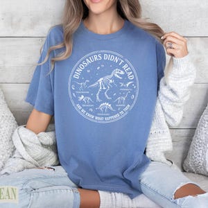 T-shirt with dinosaurs, skeleton illustrations, and text "DINOSAURS DIDN'T READ AND WE KNOW WHAT HAPPENED TO THEM".