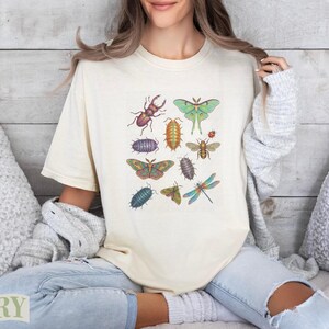 Cream t-shirt featuring an artistic arrangement of various colorful insects.