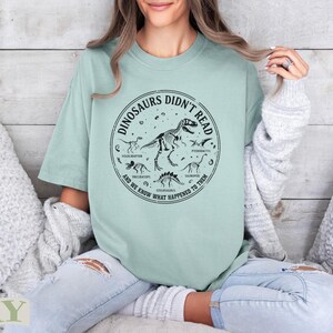 Light green t-shirt with dinosaur skeleton graphic and text "Dinosaurs Didn't Read".