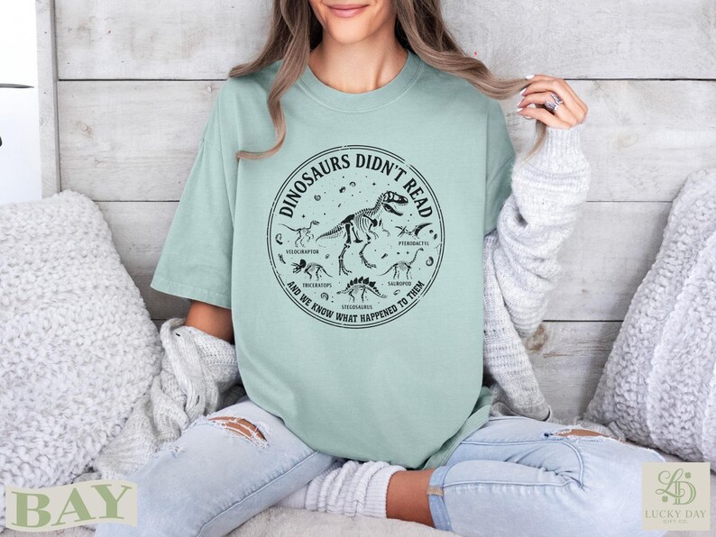 Light green t-shirt with dinosaur skeleton graphic and text "Dinosaurs Didn't Read".
