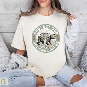 Cream t-shirt with "Protect Our National Parks" circular bear and mountain graphic.