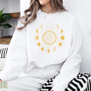 White crewneck sweatshirt with yellow celestial moon phase mandala design.