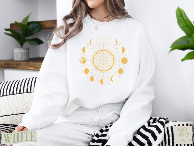 White crewneck sweatshirt with yellow celestial moon phase mandala design.