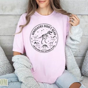 Pink t-shirt with dinosaur skeleton graphic and text "Dinosaurs Didn't Read".