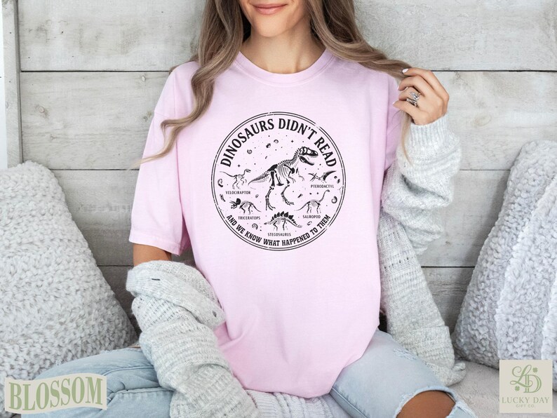 Pink t-shirt with dinosaur skeleton graphic and text "Dinosaurs Didn't Read".