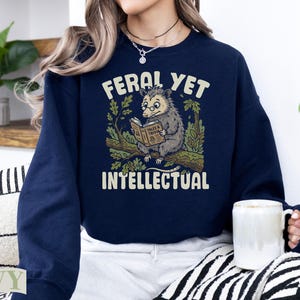 Navy sweatshirt with raccoon reading a book, "Feral Yet Intellectual" text.
