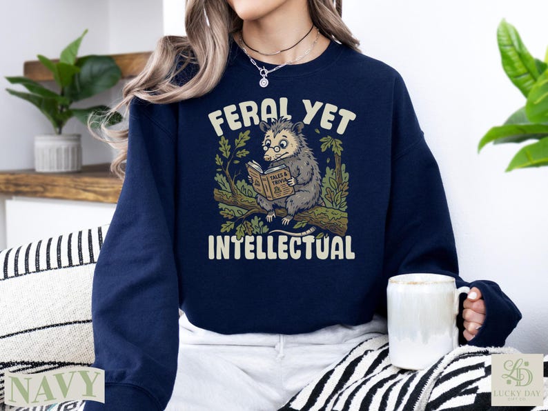 Navy sweatshirt with raccoon reading a book, "Feral Yet Intellectual" text.