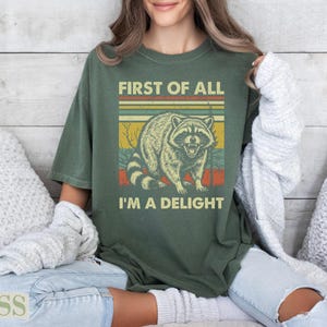 Green t-shirt with raccoon and text "First of All I'm a Delight".