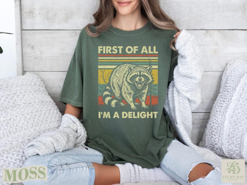 Green t-shirt with raccoon and text "First of All I'm a Delight".