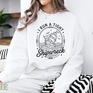 White sweatshirt with a circular graphic of a sailing ship in a storm.