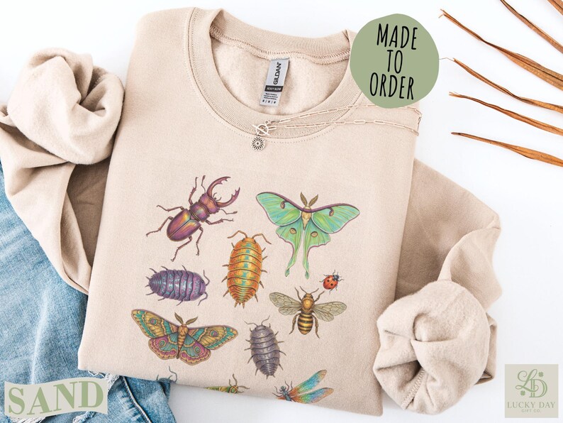 Beige sweatshirt with insects: moth, beetle, dragonfly, bee, roly-poly, and butterfly.