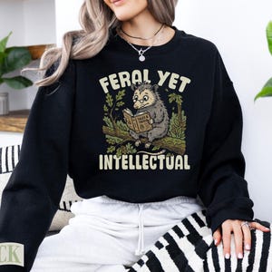 Black sweatshirt with opossum reading a book and text "FERAL YET INTELLECTUAL".