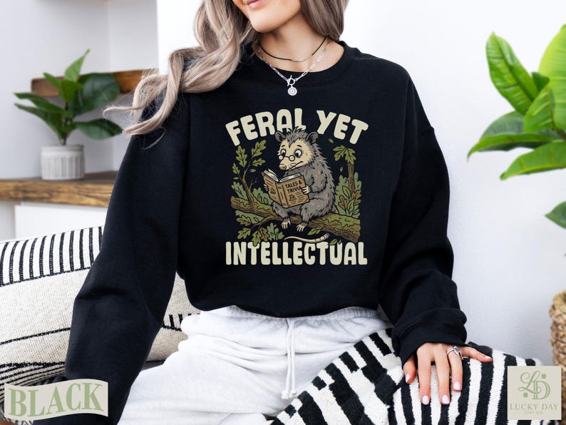 Black sweatshirt with opossum reading a book and text "FERAL YET INTELLECTUAL".
