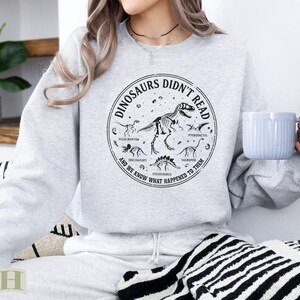 Light gray sweatshirt with dinosaur skeletons and text "Dinosaurs Didn't Read".