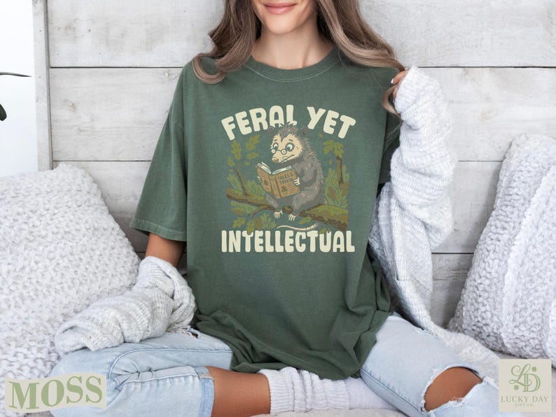 Olive green t-shirt with opossum reading a book, "Feral Yet Intellectual."