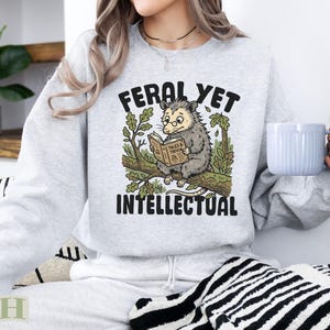 Feral Yet Intellectual sweatshirt with opossum reading book on branch.