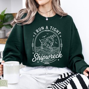 Dark green sweatshirt with "I RUN A TIGHT SHIPWRECK" nautical graphic.