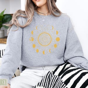 Grey sweatshirt with yellow celestial moon phase graphic.