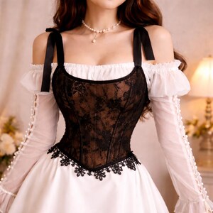 May include: A black lace corset over a white dress. The corset has a floral pattern and black ribbon straps. The dress features long, sheer sleeves with pearl accents and a ruffled neckline. A pearl necklace is also visible.