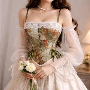 May include: A floral print corset with green straps and a white lace trim. The corset features a delicate floral pattern in shades of green, brown, and white. The sleeves are sheer and the dress is a cream color.