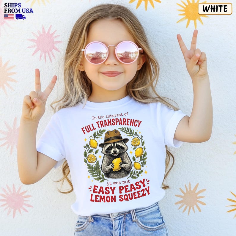 May include: A white t-shirt featuring a graphic of a raccoon wearing a brown fedora and holding a yellow lemon. The text reads In the interest of FULL TRANSPARENCY it was not EASY PEASY LEMON SQUEEZY, surrounded by green leaves and yellow lemons.