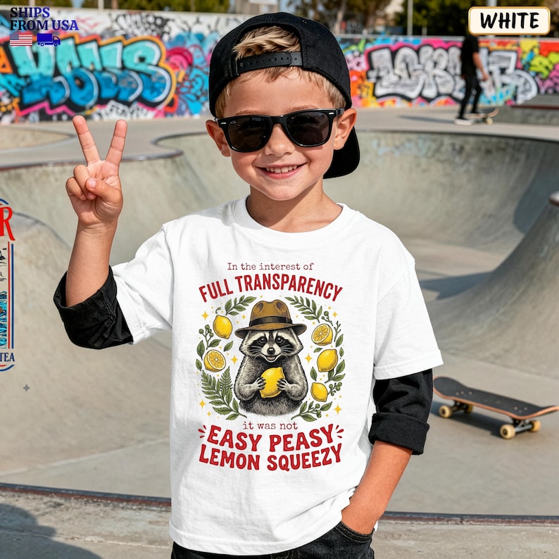 May include: A white short-sleeved t-shirt featuring a graphic of a raccoon wearing a brown fedora and holding a yellow lemon. The text reads In the interest of FULL TRANSPARENCY it was not EASY PEASY LEMON SQUEEZY, surrounded by green leaves.
