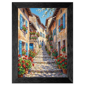 May include: Framed art print depicting a European village street scene. The artwork features stone buildings with blue shutters and doors, adorned with red geraniums in pots. A cobblestone street leads into the distance under a blue sky.