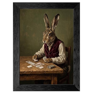May include: Framed art print featuring a rabbit dressed in a vest and shirt, playing cards at a wooden table. The rabbit is the focal point, with a deck of cards and a green background. The print is in a black frame.