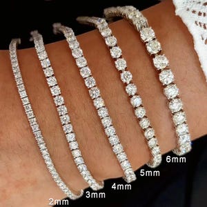 May include: A collection of diamond tennis bracelets in various sizes. The bracelets range from 2mm to 6mm in width, each showcasing a line of sparkling, round-cut diamonds. The image highlights the different sizes available, perfect for layering or wearing individually.
