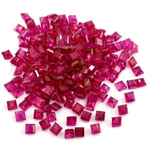 Könnte beinhalten: Ein Haufen quadratisch geschliffener Rubine in verschiedenen Größen. Die Edelsteine haben eine tiefe, satte rote Farbe, wobei die Facetten das Licht einfangen. Das Bild ist vor einem weißen Hintergrund aufgenommen, was die Brillanz der Edelsteine hervorhebt.