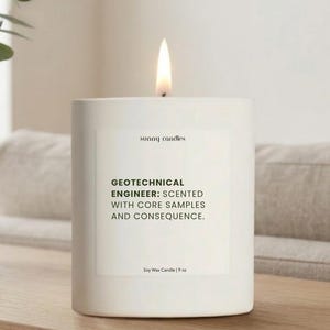 May include: A lit white soy wax candle with the text "GEOTECHNICAL ENGINEER: SCENTED WITH CORE SAMPLES AND CONSEQUENCE." The candle is 9 oz.