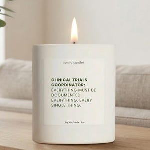 May include: A lit white soy wax candle with the text "CLINICAL TRIALS COORDINATOR: EVERYTHING MUST BE DOCUMENTED. EVERYTHING. EVERY SINGLE THING." The candle is 9 oz and has the words "sunny candles" printed on it.